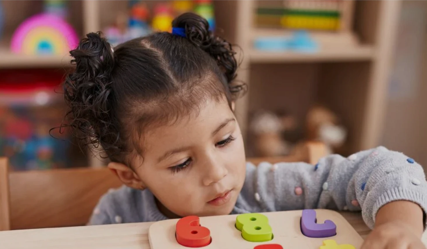 Young child placing coloured wooden number pieces into a puzzle board in a Montessori classroom