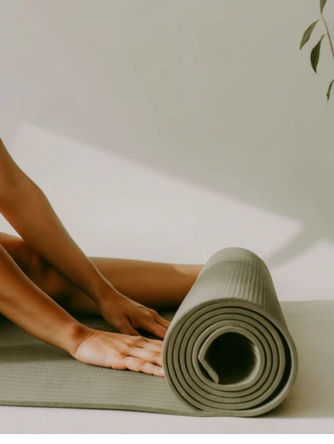 Hands smoothing a sage green yoga mat in soft daylight