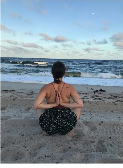 Seated practice on the beach at dusk with hands in prayer behind the back